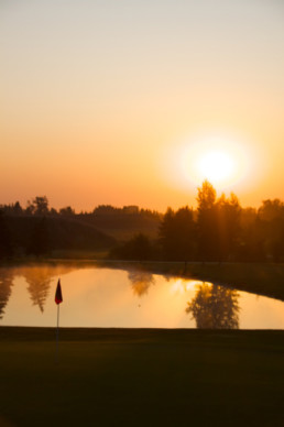 sun setting over water hazard and hole flag at The Links at Spruce Grove